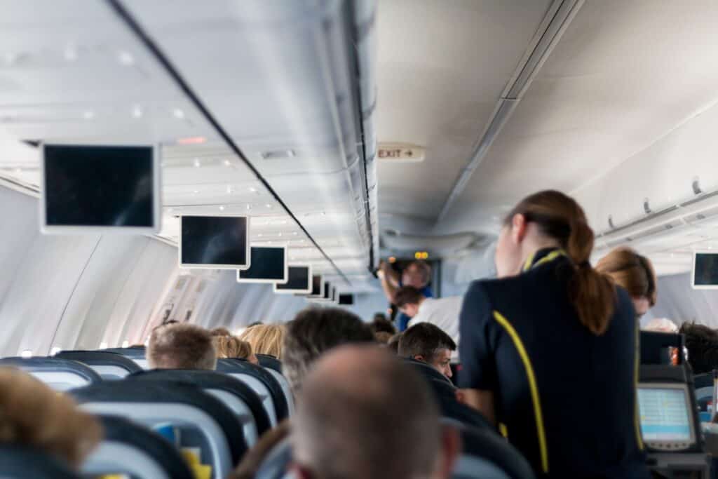 Man erkennt den Innenraum eines Flugzeuges. Im Vordergrund wird ein Fluggast durch eine Stewardess bedient.