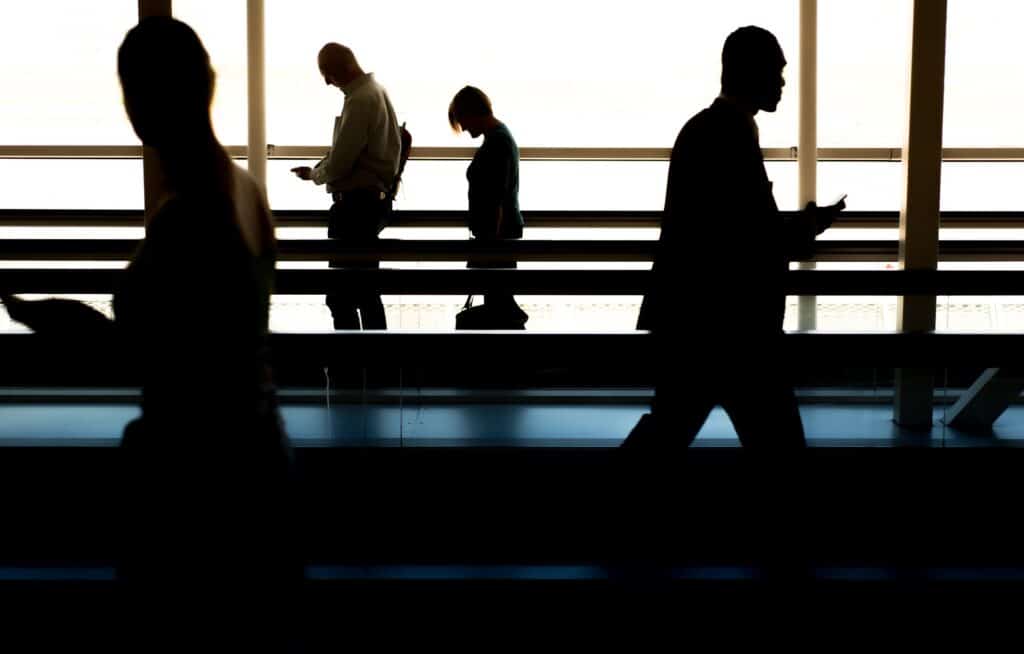 Es sind mehrere Menschen am Flughafen zu sehen, die auf ihr Handy gucken. Was ist bei Flugannullierung?