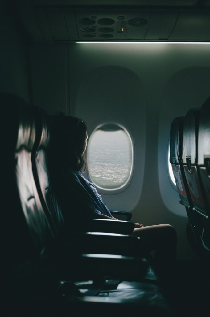 Man sieht eine Frau am Fenster eines Flugzeuges. Sie schaut aus dem Fenster.
