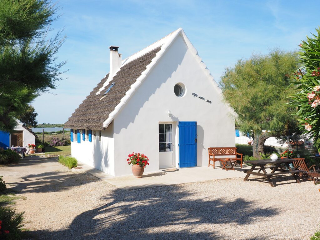 Man sieht ein weißes Ferienhaus mit Hof vor blauem Himmel.