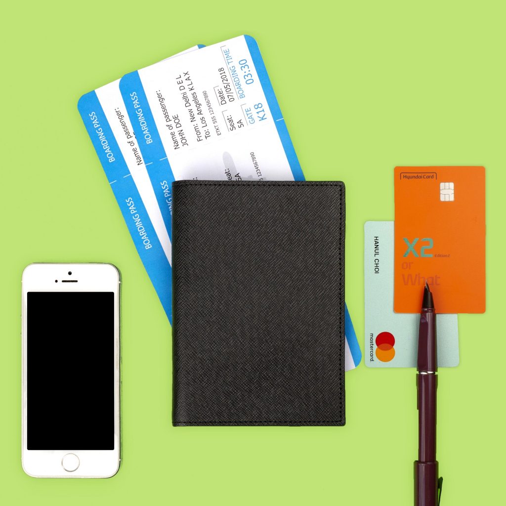 Zu sehen ist ein Smartphone, ein Heft mit Flugtickets, zwei Bankkarten und einem Kugelschreiber.