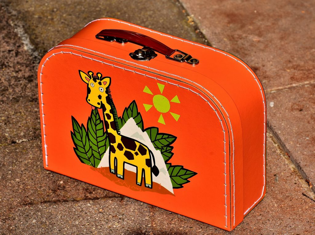 Man sieht einen orangen Kinderkoffer mit einem Giraffenmotiv.