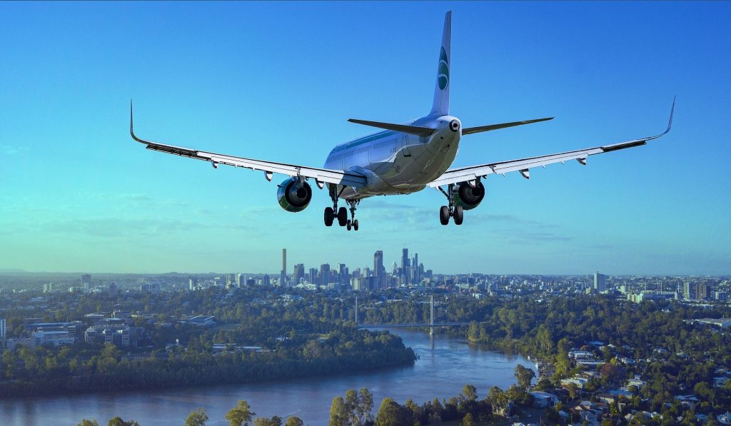 Man sieht ein Flugzeug im Landeanflug auf Frankfurt vor blauem Himmel. Es ist ein Fluß und die Skyline Frankfurts zu sehen.