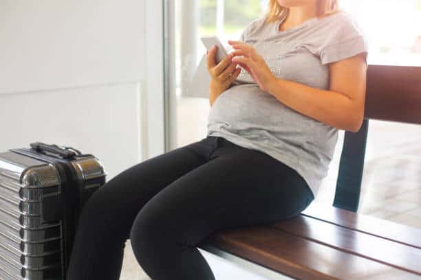 Sitzende schwangere Frau am Flughafen vor dem Fliegen