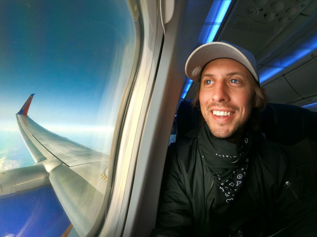 Ein Mann der lachend den Fensterplatz im Flugzeug bekommen hat