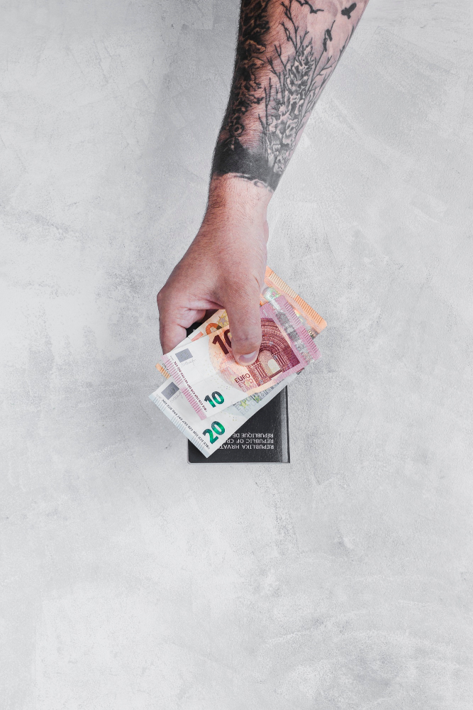 Ein tattowierter Arm mit Euroscheinen und Pass in der Hand.