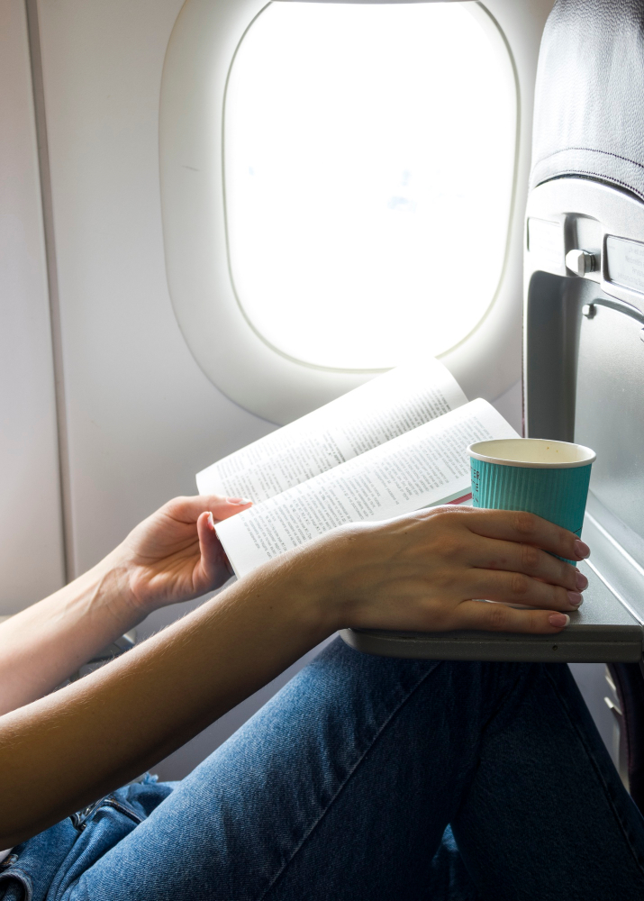 Fensterplatz im Flugzeug mit Kaffee und Buch.