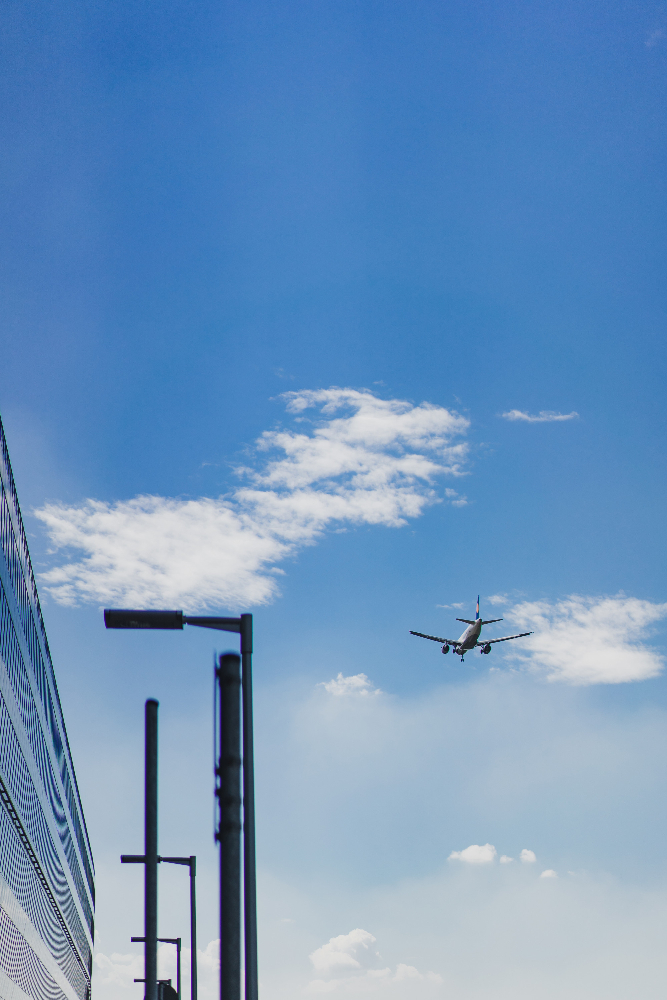 Links ein Flughafengebäude, rechts ein Flugzeug vor blauem Himmel.