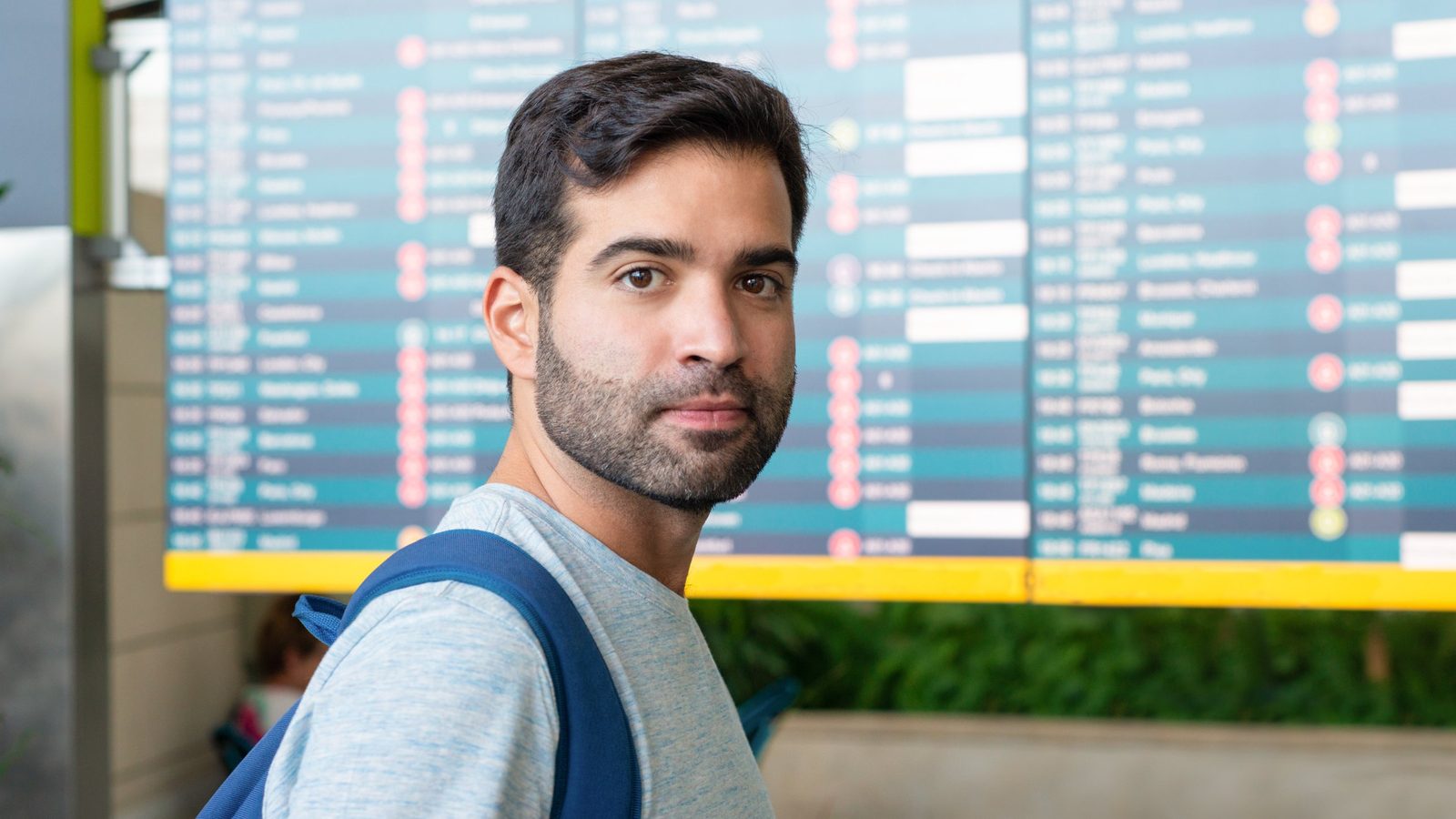 Reisender mit Rucksack vor der Anzeigetafel am Flughafen