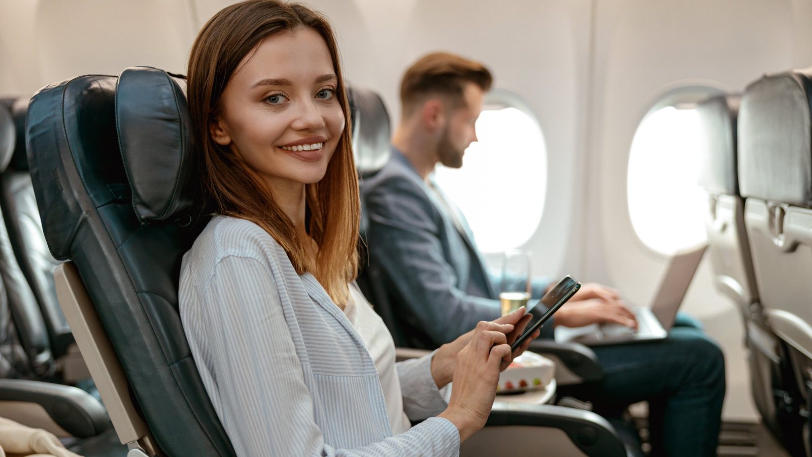Lächelnde Reisende mit Smartphone im Flugzeug